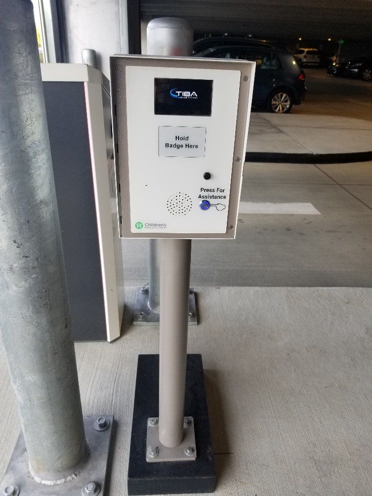 Controlled access system at the entry of secure parking garage with scanner access and button for assistance.