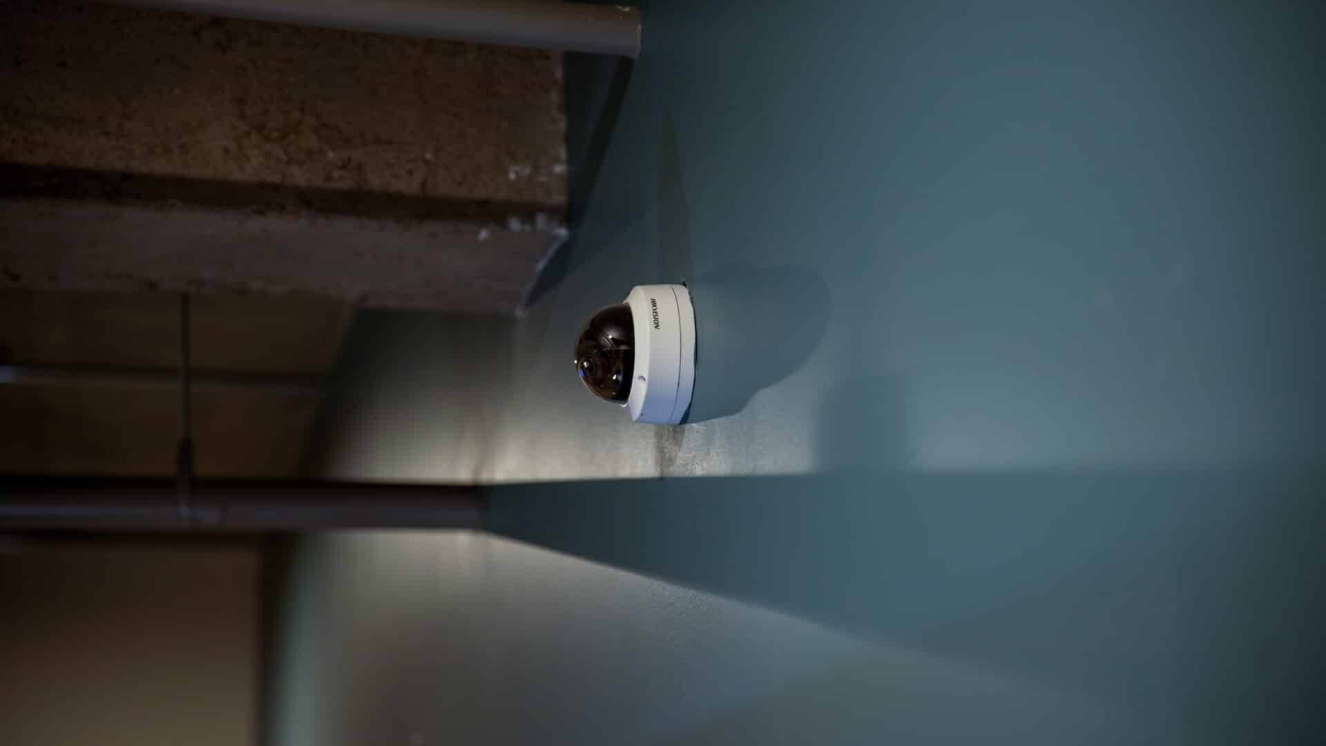 White and black wall security camera mounted on a blue exterior wall.