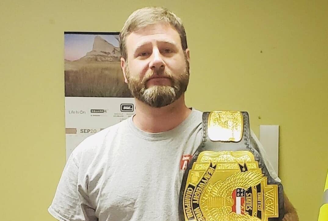 Anderson Evan, Heavyweight Wrestling Champion, stands holding a large belt.