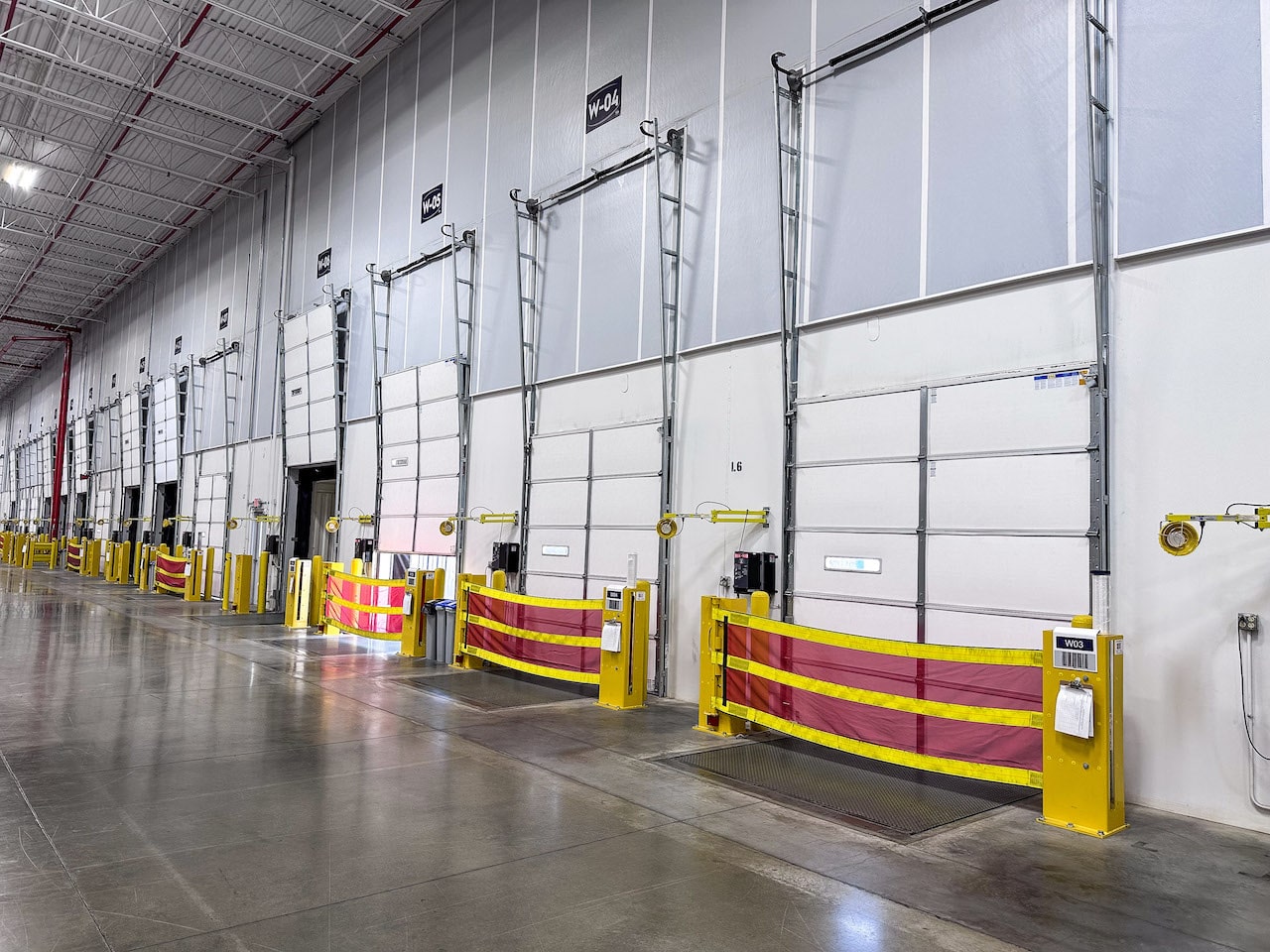 Inside of an industrial space with a row of white overhead doors with number tag on the above