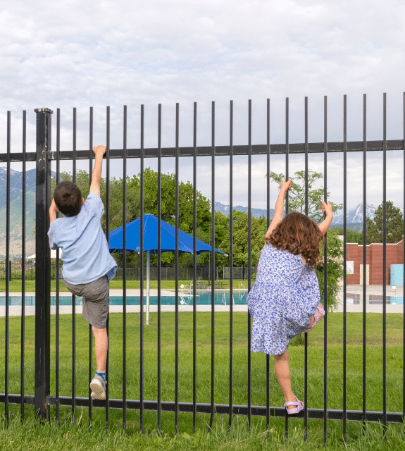 Children trying to climb metal fence surrounding pool