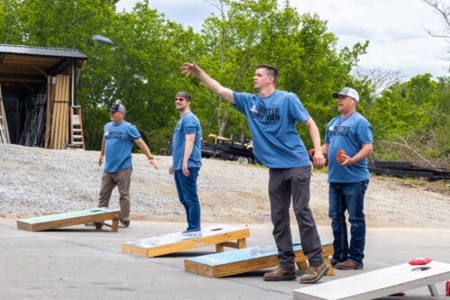 Guardian Access Solutions team members wearing blue shirts play a game of corn hole.